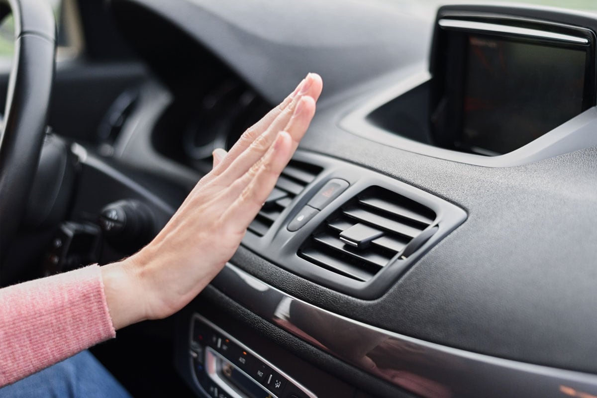 Woman hand on air conditioner ventilation grille in car
