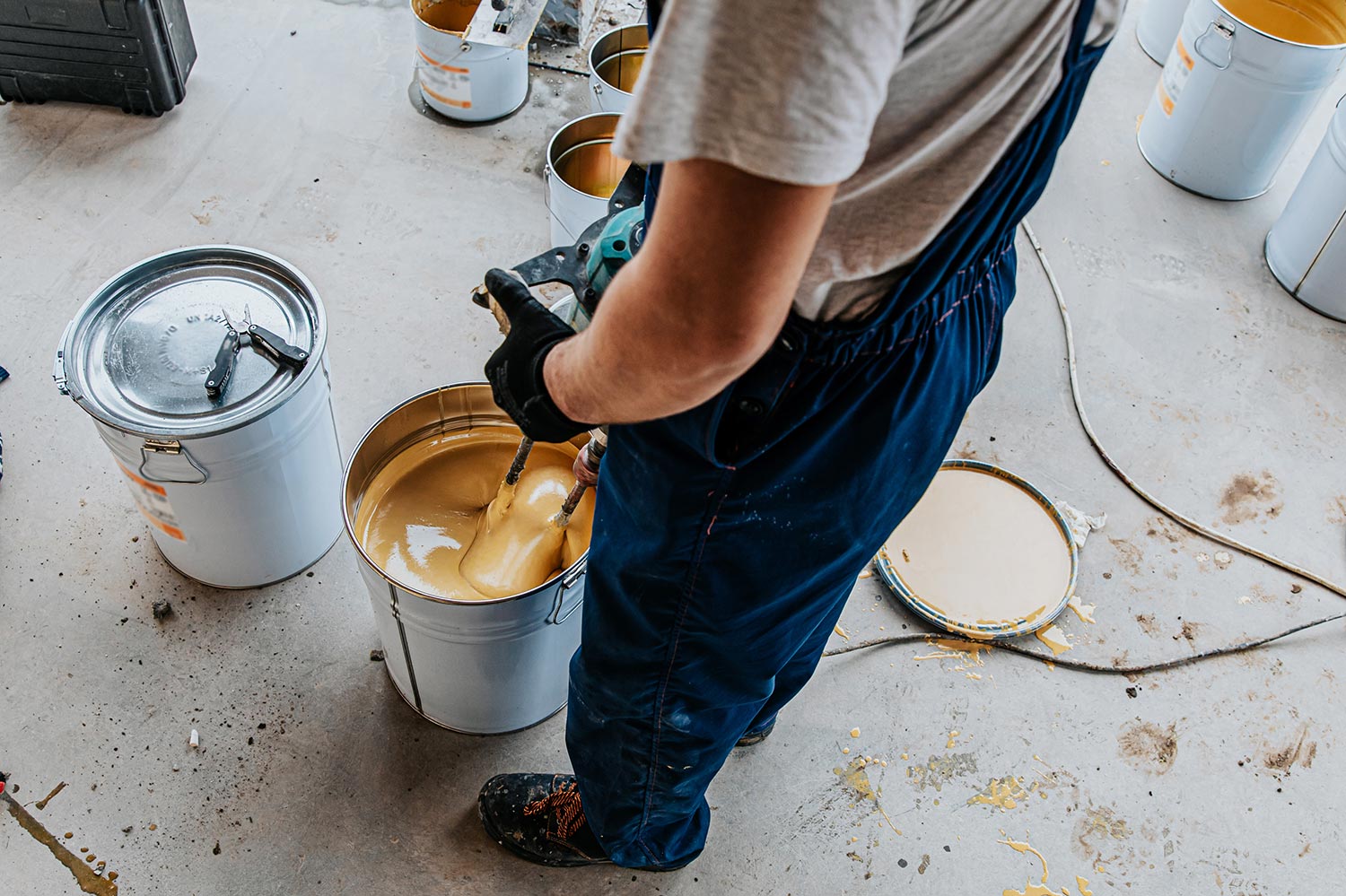 Worker mixing yellow epoxy resin with the mixer in a tin bucket