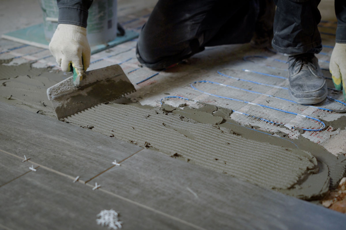 Worker putting adhesive on the floor for placing tiles