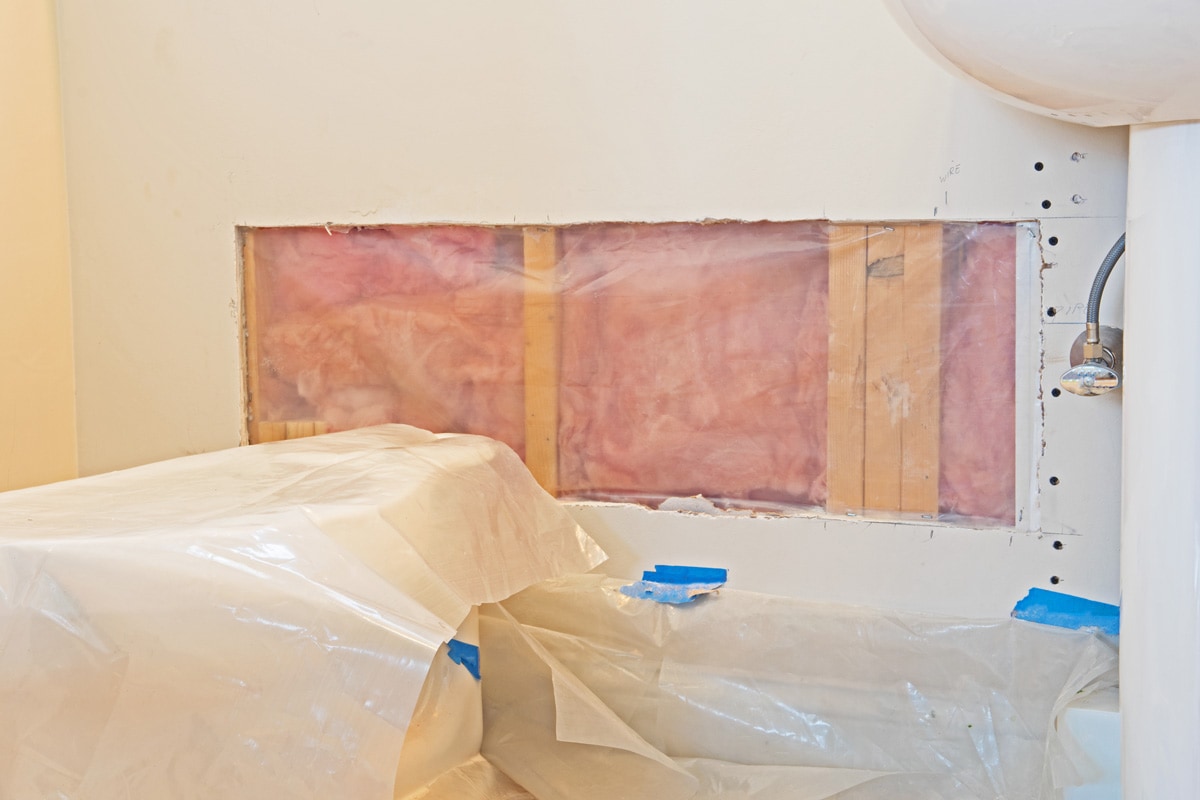 a hole in the drywall has been prepared for patching and a sheet of plastic placed over the insulation to act as a vapor barrier.
