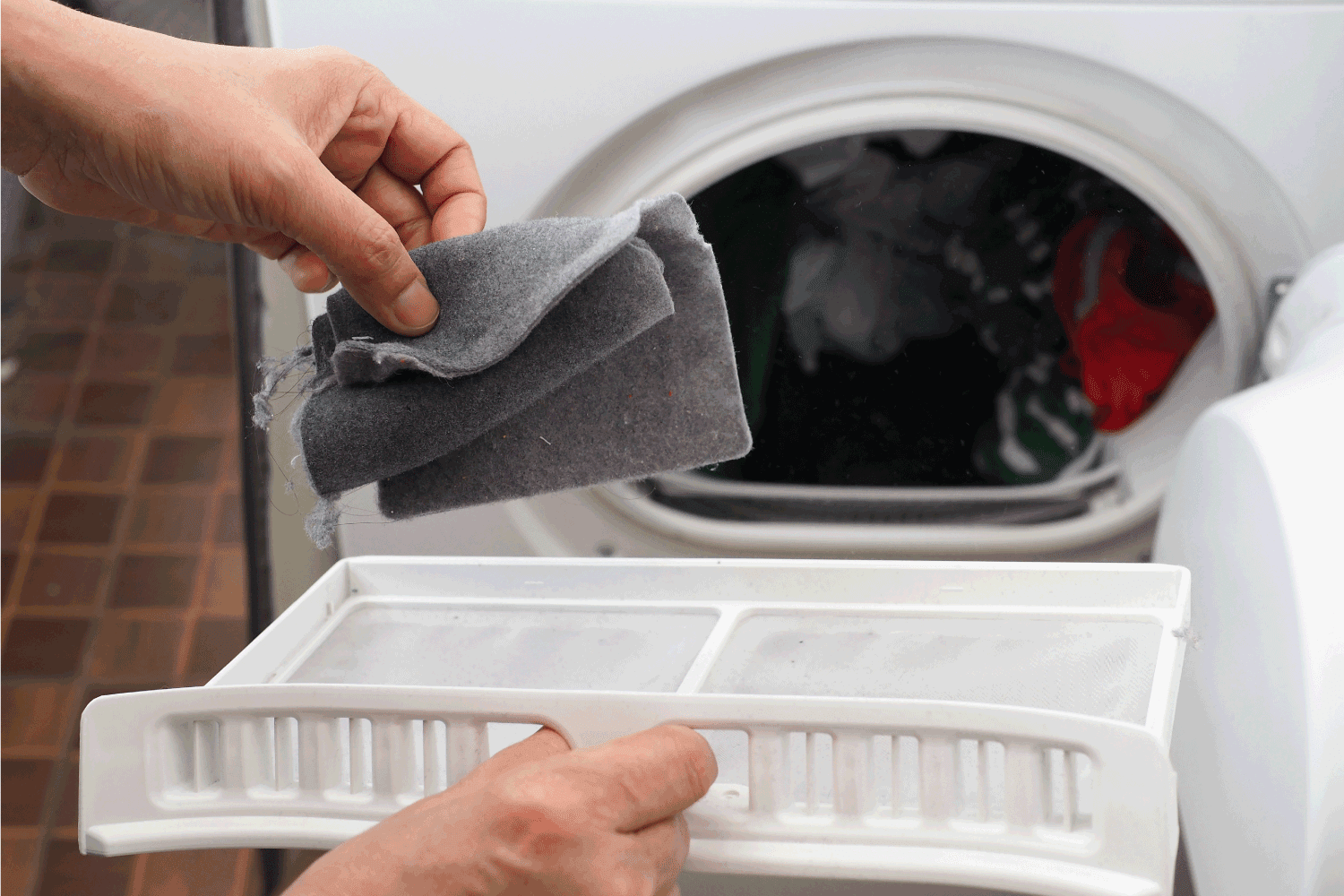 hand removing lint from fluff filter of the tumble dryer on blurred background of clothes dryer with washed clothing