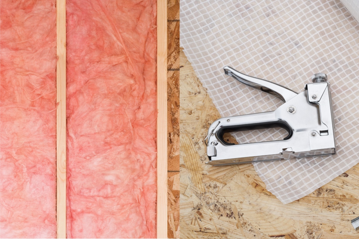 pink fiberglass insulation installed on wall panel. plastic sheet vapor barrier and stapler gun. How To Install Fiberglass Insulation With Vapor Barrier