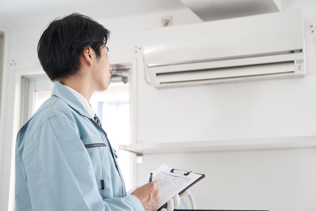A Japanese male electrician checking a home air conditione