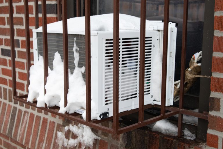 A window air conditioner in a barred cage with snow on a brick urban building in New York City, How Do I Cover My Wall Air Conditioner For Winter?