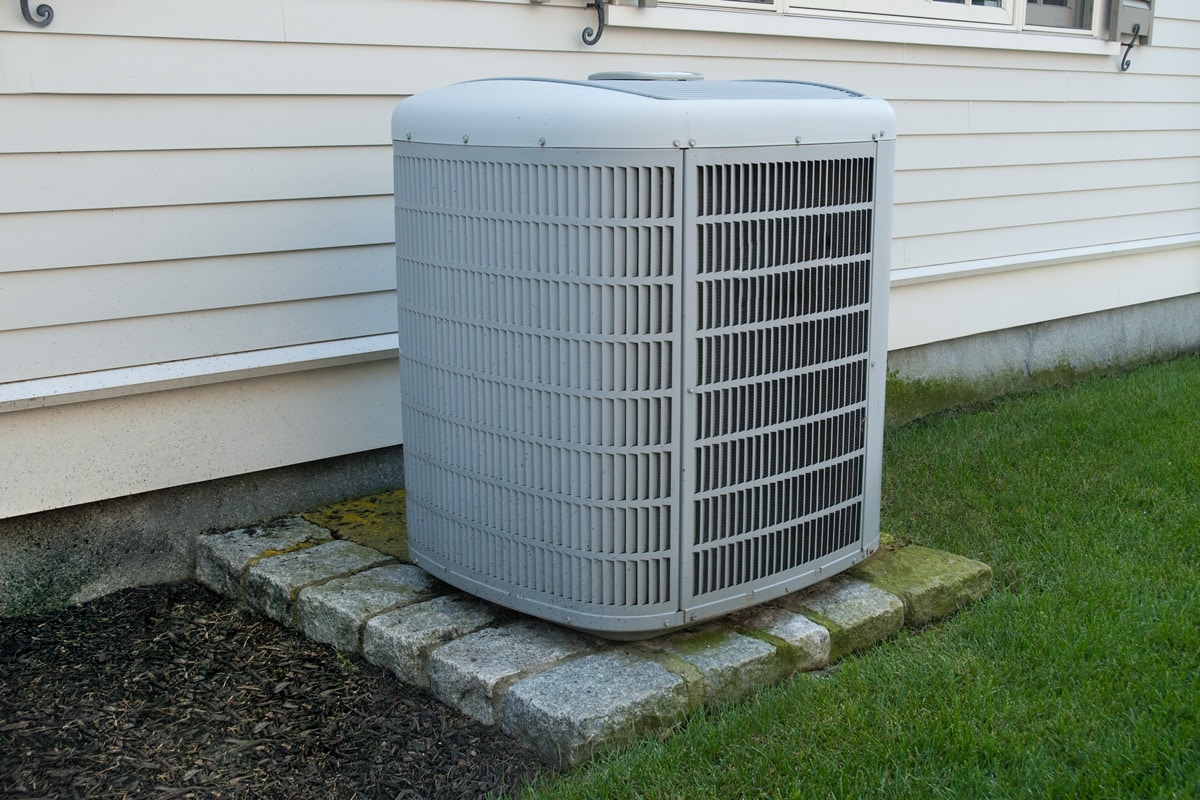 An air conditioning unit mounted on concrete bricks at the backyard of the house