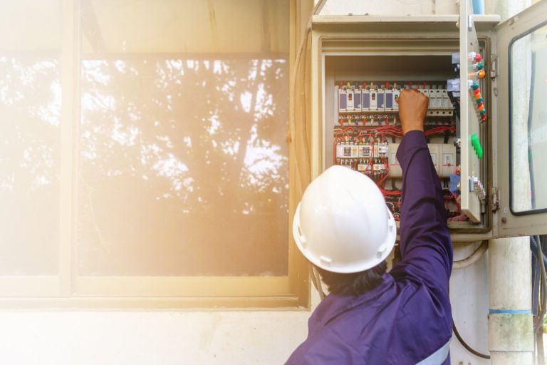 Back of asian engineer or technician in safety uniform and white security helmet turning on switch in the electrical cabinet with copy space and sun light effect for industrial concept - Does A Furnace Need A Dedicated Circuit?