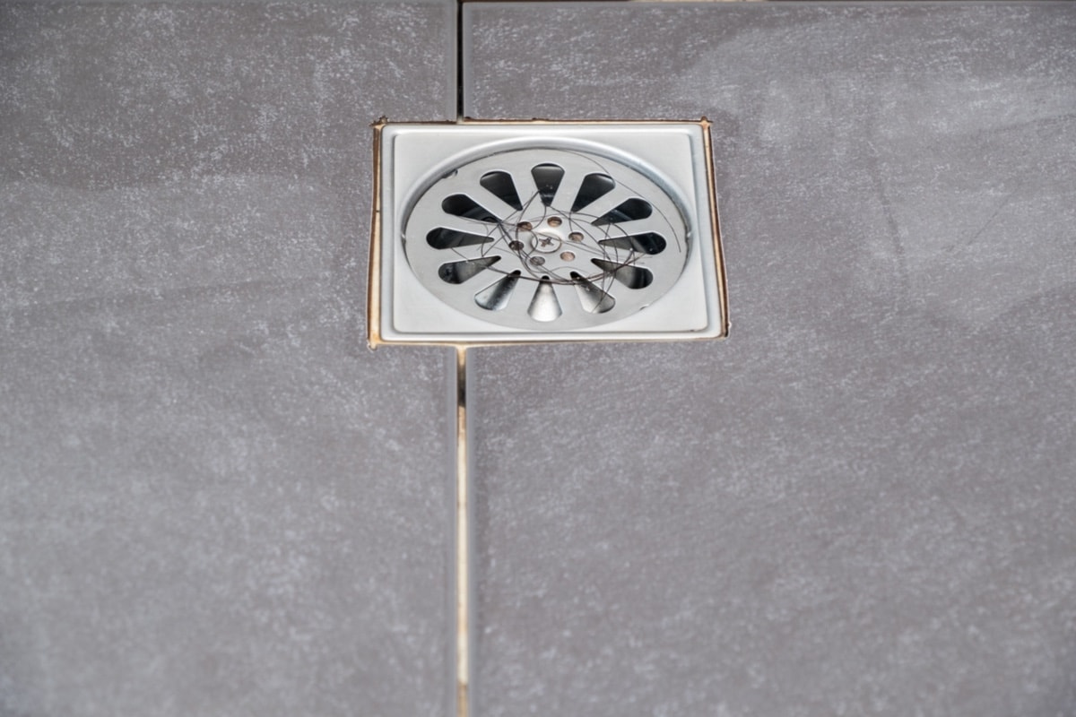 Blocked Drain hole - The hair loss clogs the metal drain cover on the black floor tiles in the shower room
