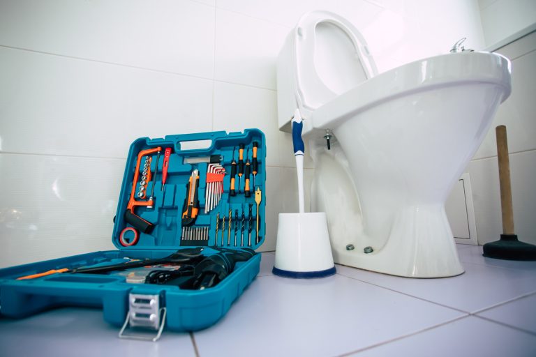 Close up photo of ceramic bowl toilet in domestic bathroom with a box of tools - Toilet Cemented To Floor - How To Remove