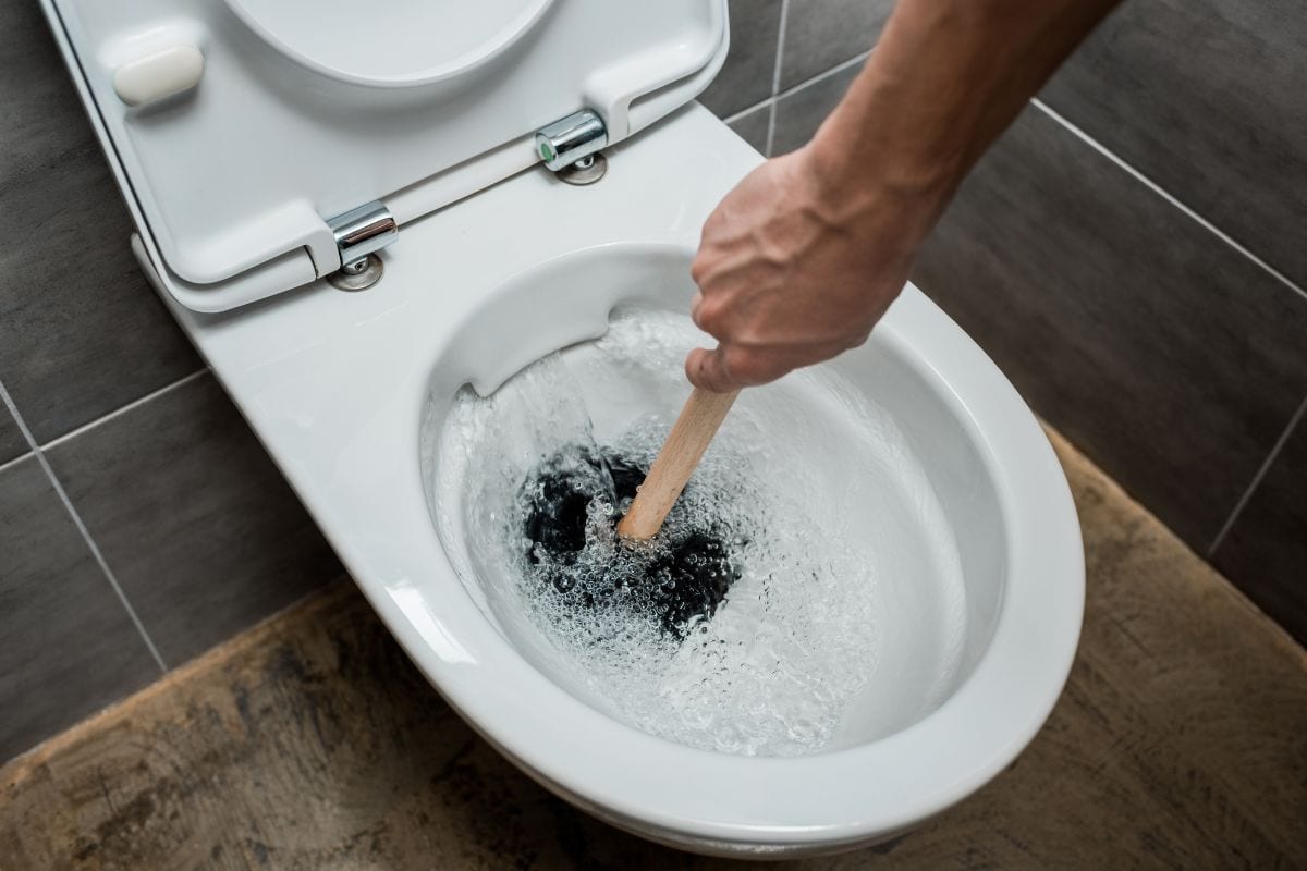Cropped view of plumber using plunger in toilet bowl during flushing in modern restroom with grey tile — Photo