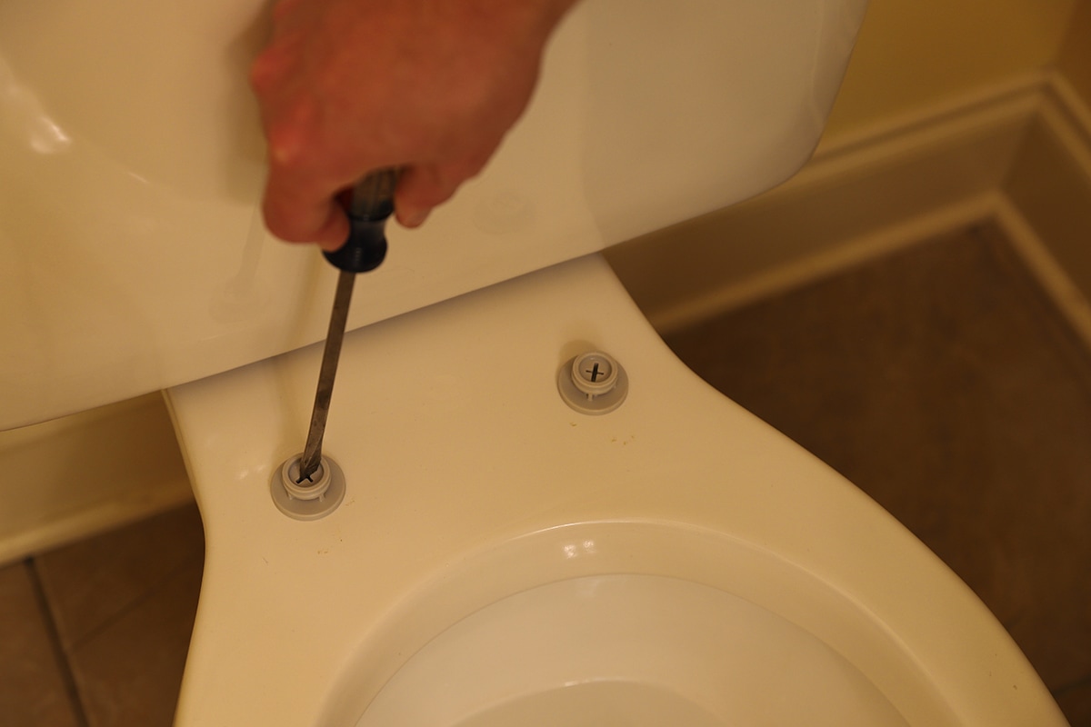 Hand working on screws to hold toilet seat onto toilet