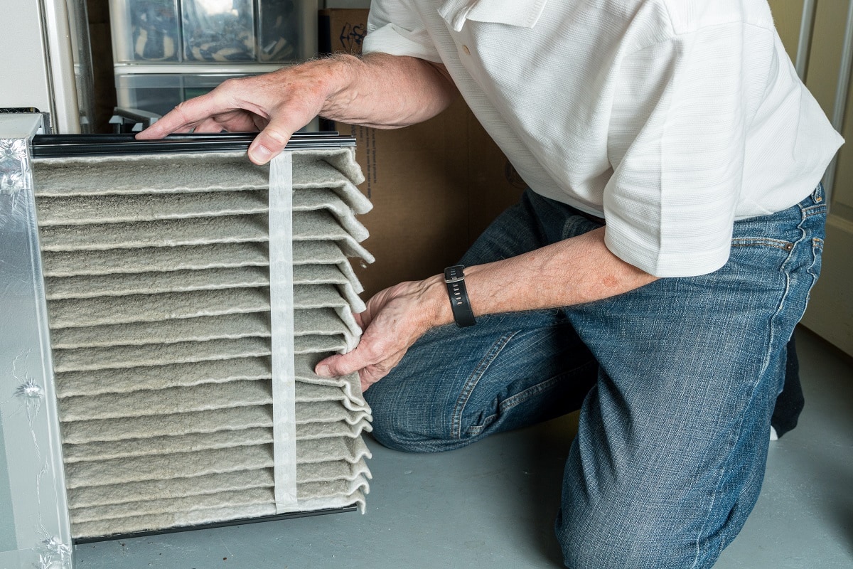 How To Replace The Air Filter - Senior caucasian man changing a folded dirty air filter in the HVAC furnace system