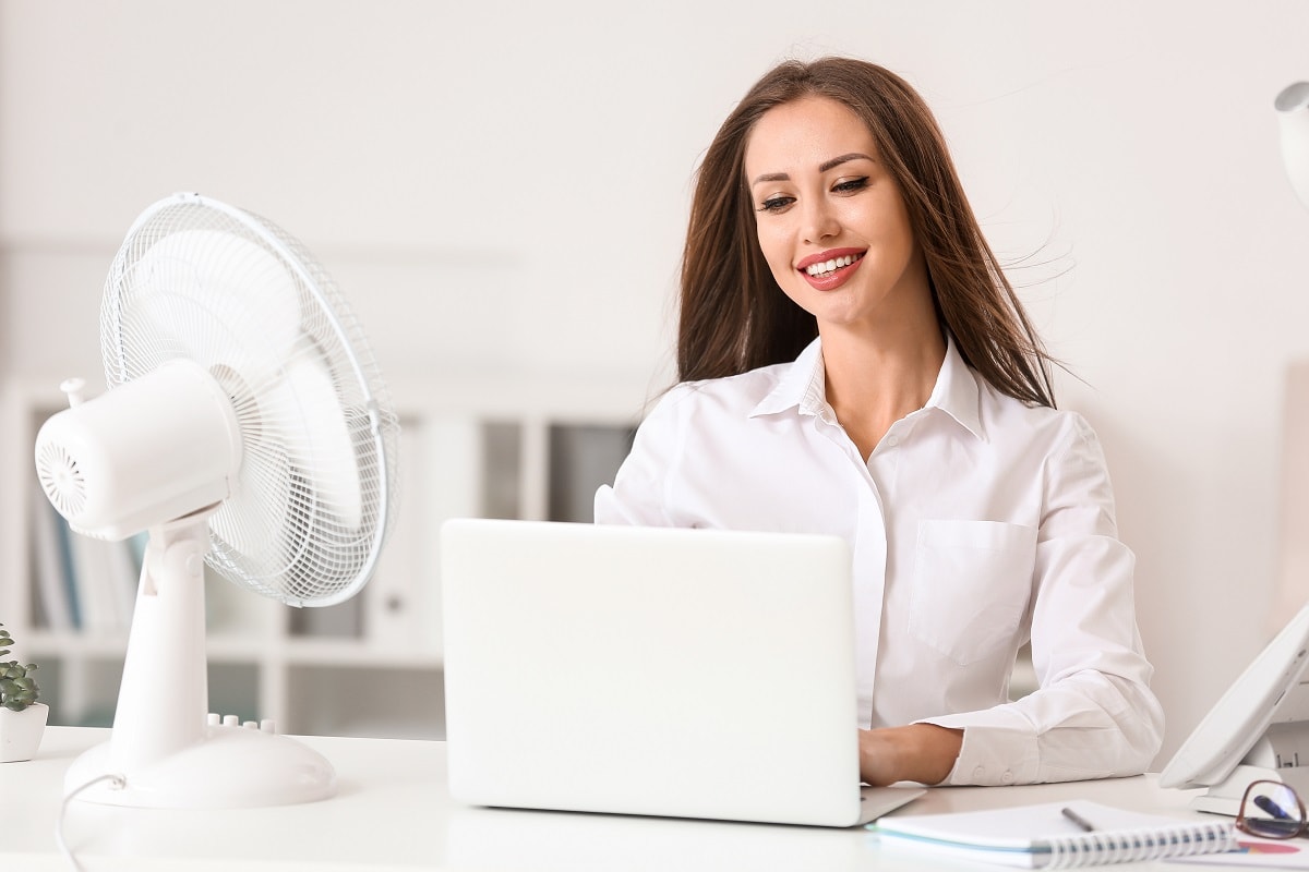 In review - Young woman using electric fan during heatwave in office