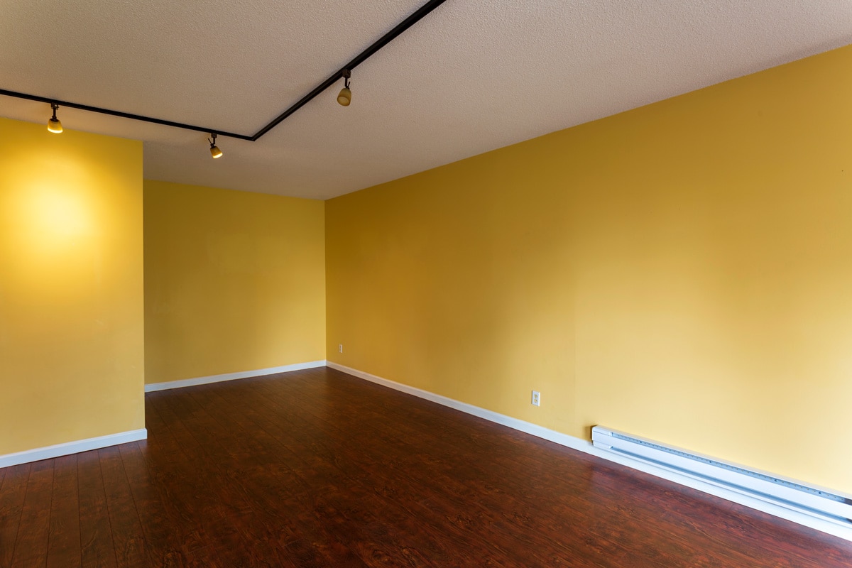 Interior of an empty yellow painted living room with spotlight lighting, white baseboard and a baseboard heater