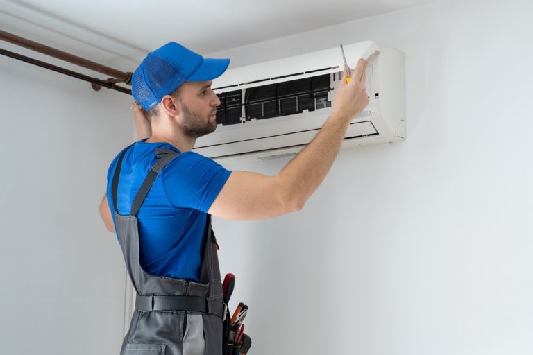 Male technician in overalls and a blue cap repairs an air conditioner on the wall, AC Works During The Day But Not At Night - What Could Be Wrong?