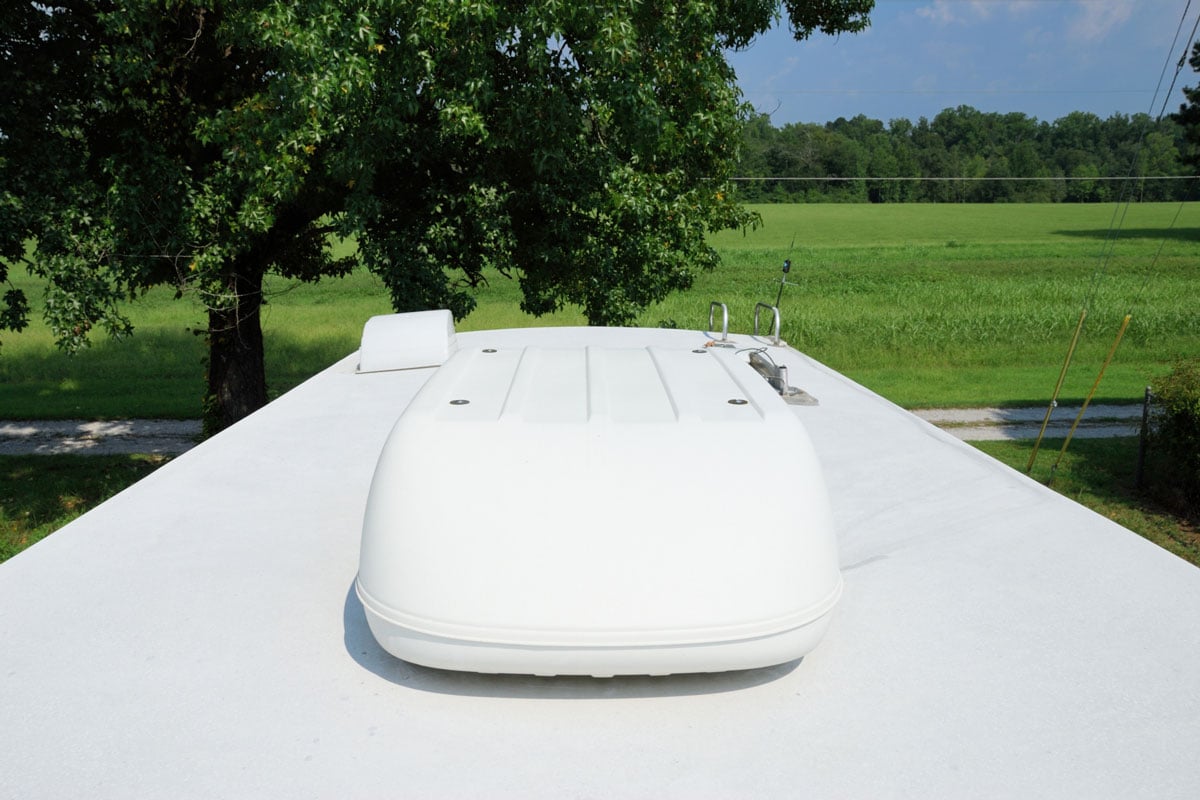 Photograph on roof of recreational vehicle looking into large field. RV roof has large air conditioning unit