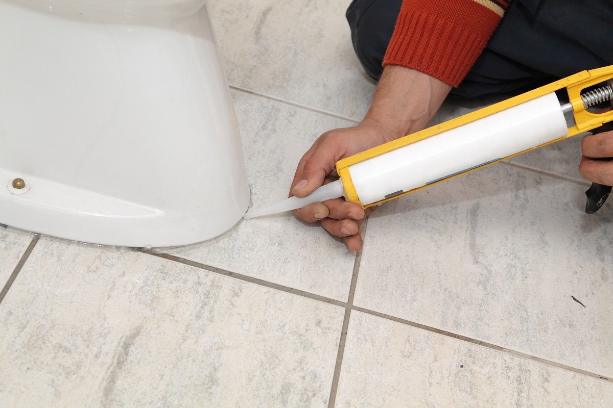 Plumber fixing toilet in a washroom with silicone cartridge