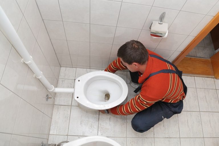 Plumber replacing broken toilet in a washroom, Toilet Not Sitting Flat On Floor - What To Do
