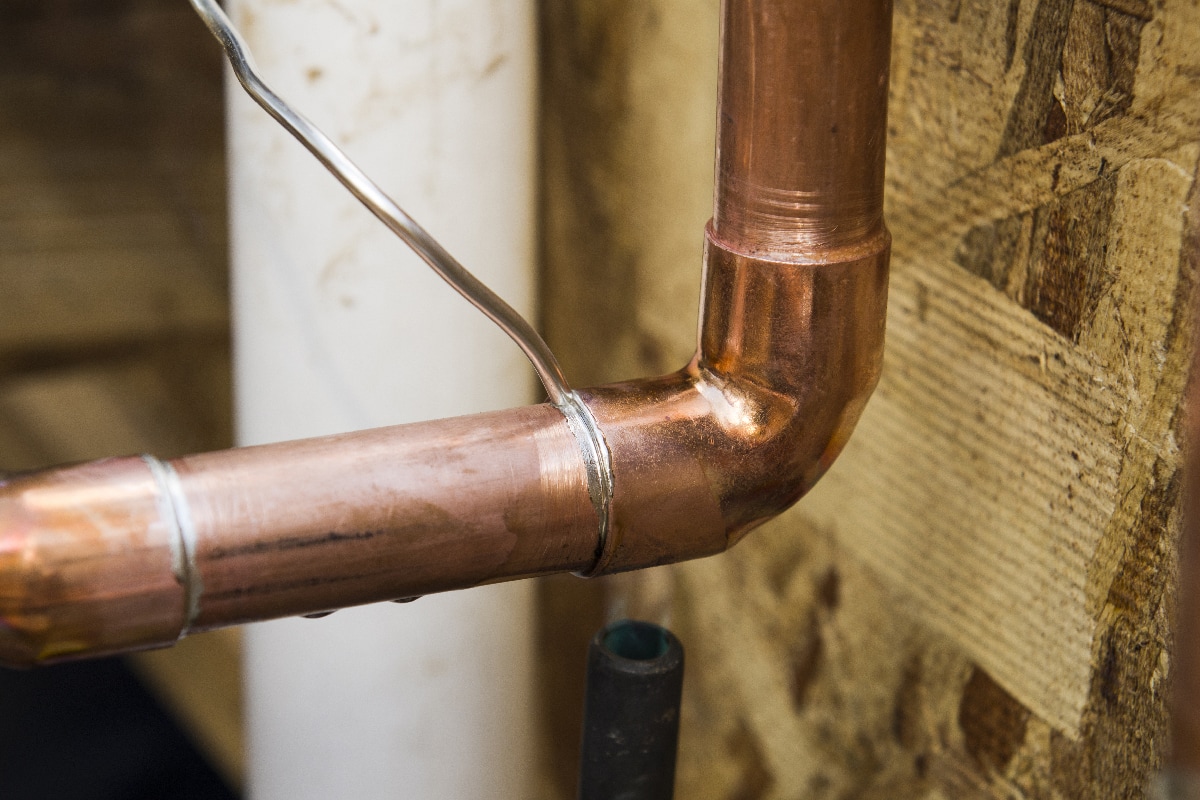 Plumbing contractor works sweating the joints on the copper pipe domestic water system