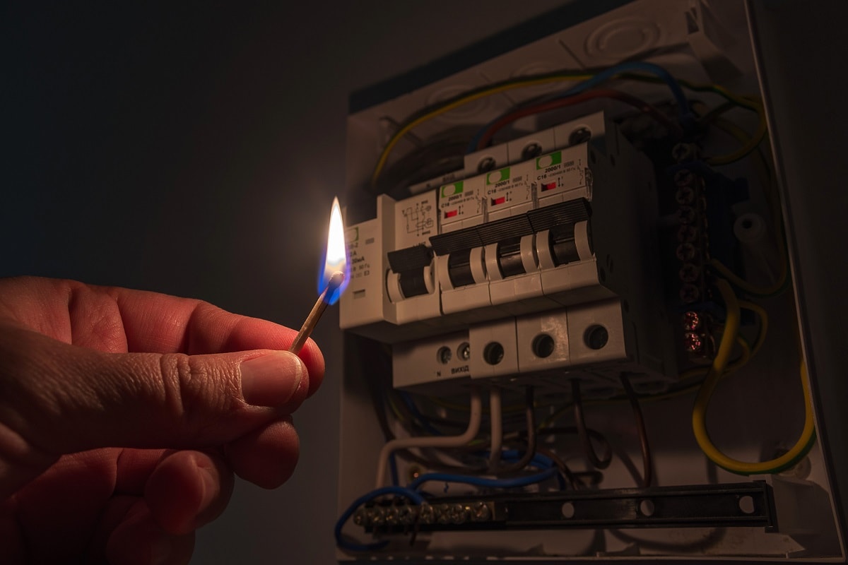 Power Outage - Blackout concept. Person's hand in complete darkness holding a burning match to investigate a home fuse box during a power outage