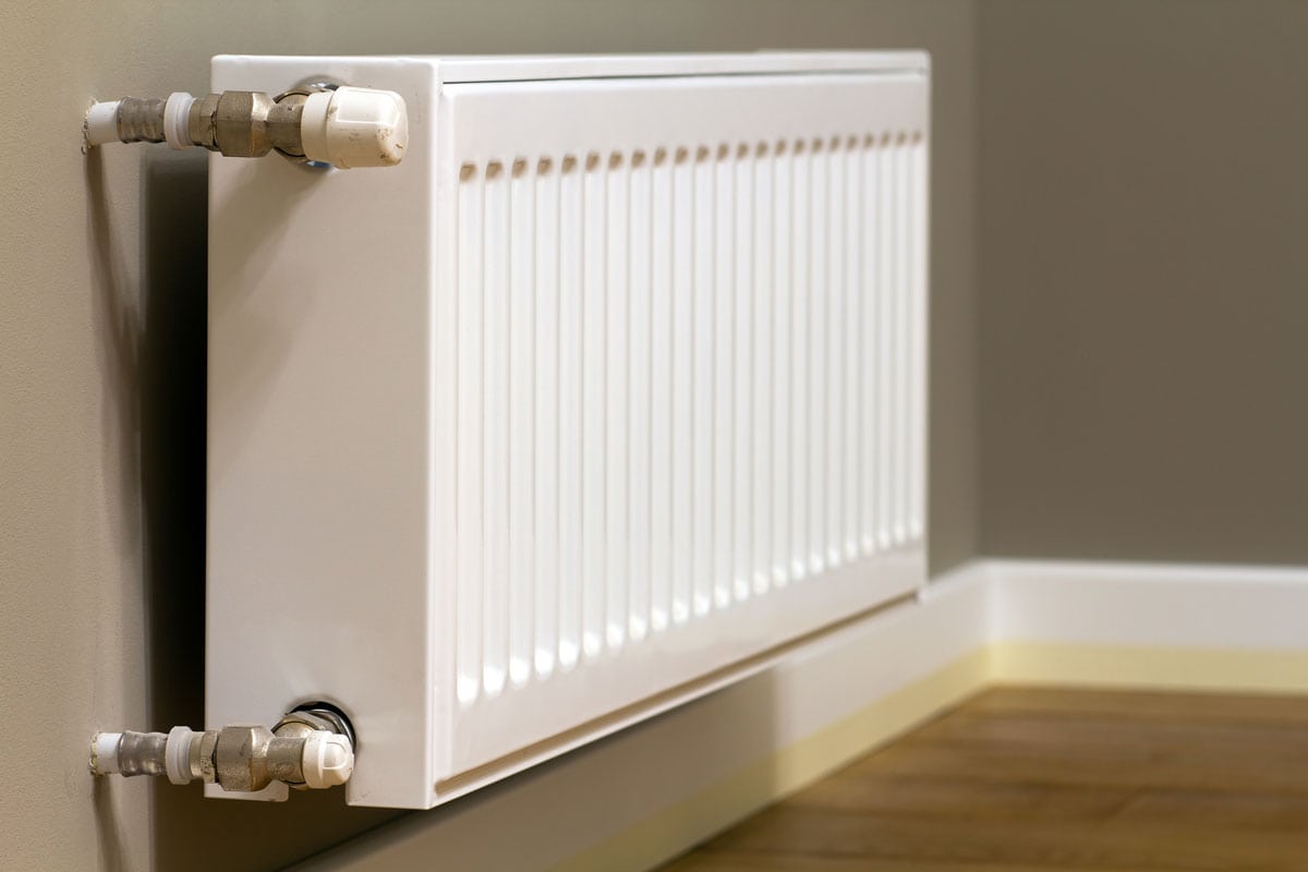 White metal heating radiator mounted on gray wall inside a room