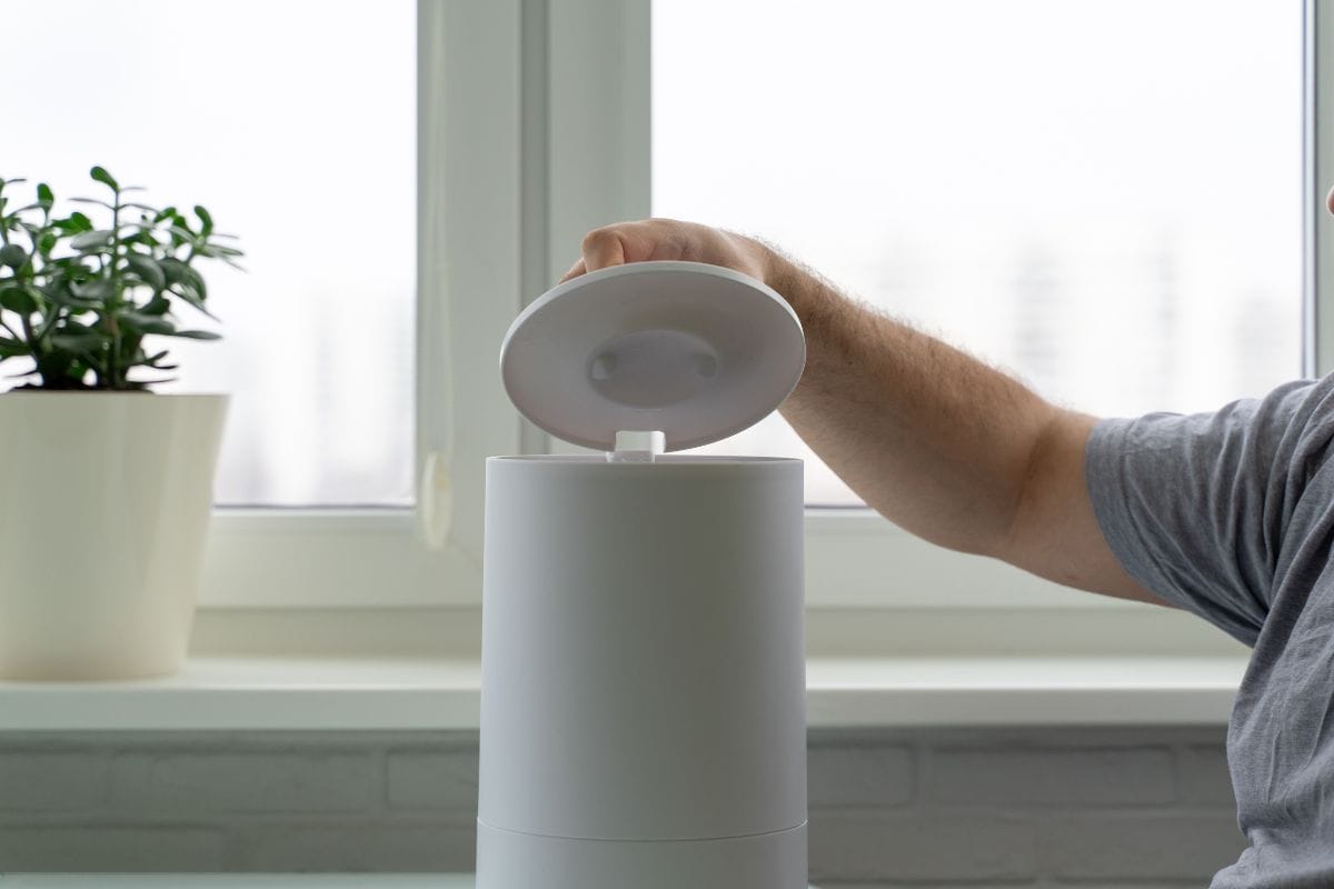 a man opens the lid of a humidifier to fill it with water. using a humidifier at home