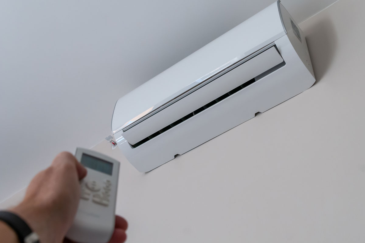 a man's hand holds the remote control of a wall-mounted air conditioner