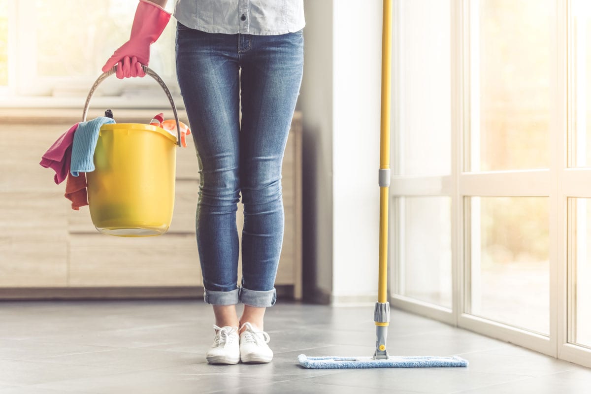 beautiful woman in protective gloves holding a flat wet-mop and bucket with detergents and rags while cleaning h