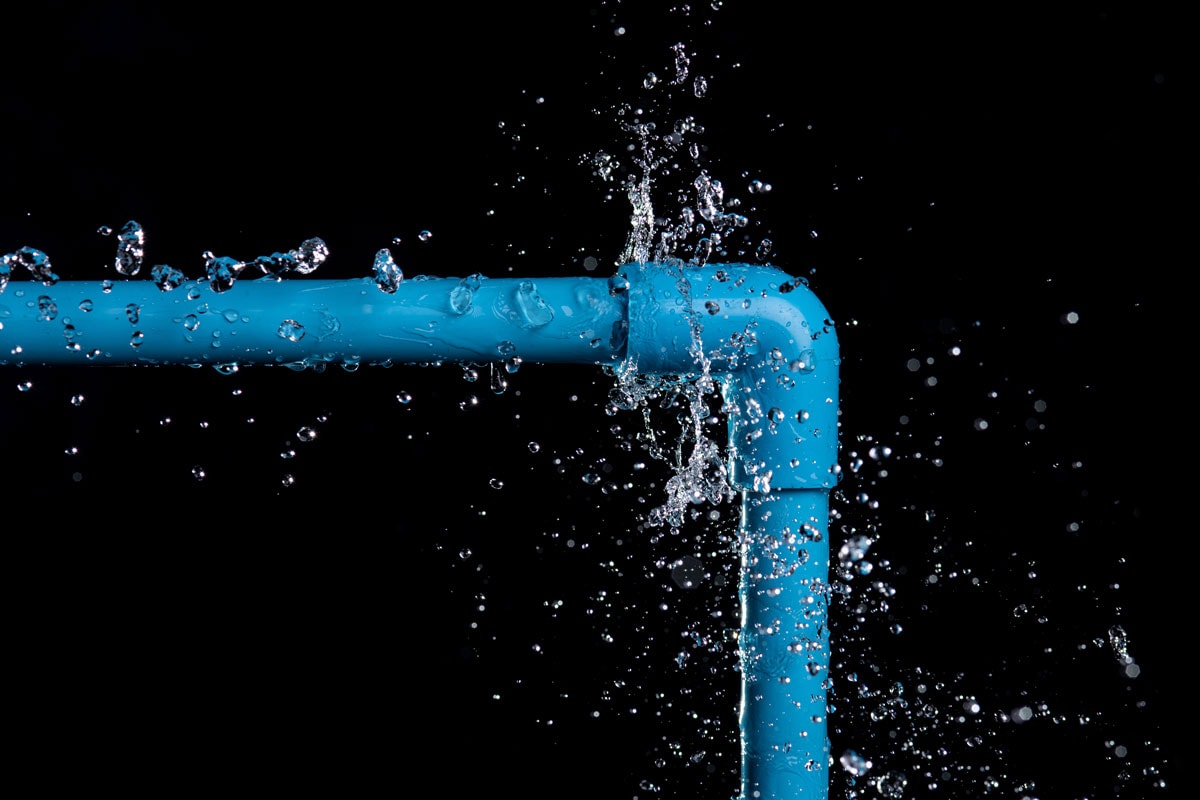 close up photo of a blue pvc water pipe water drops splashing on a black background