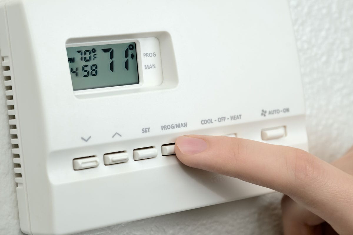 finger pressing button on digital thermostat