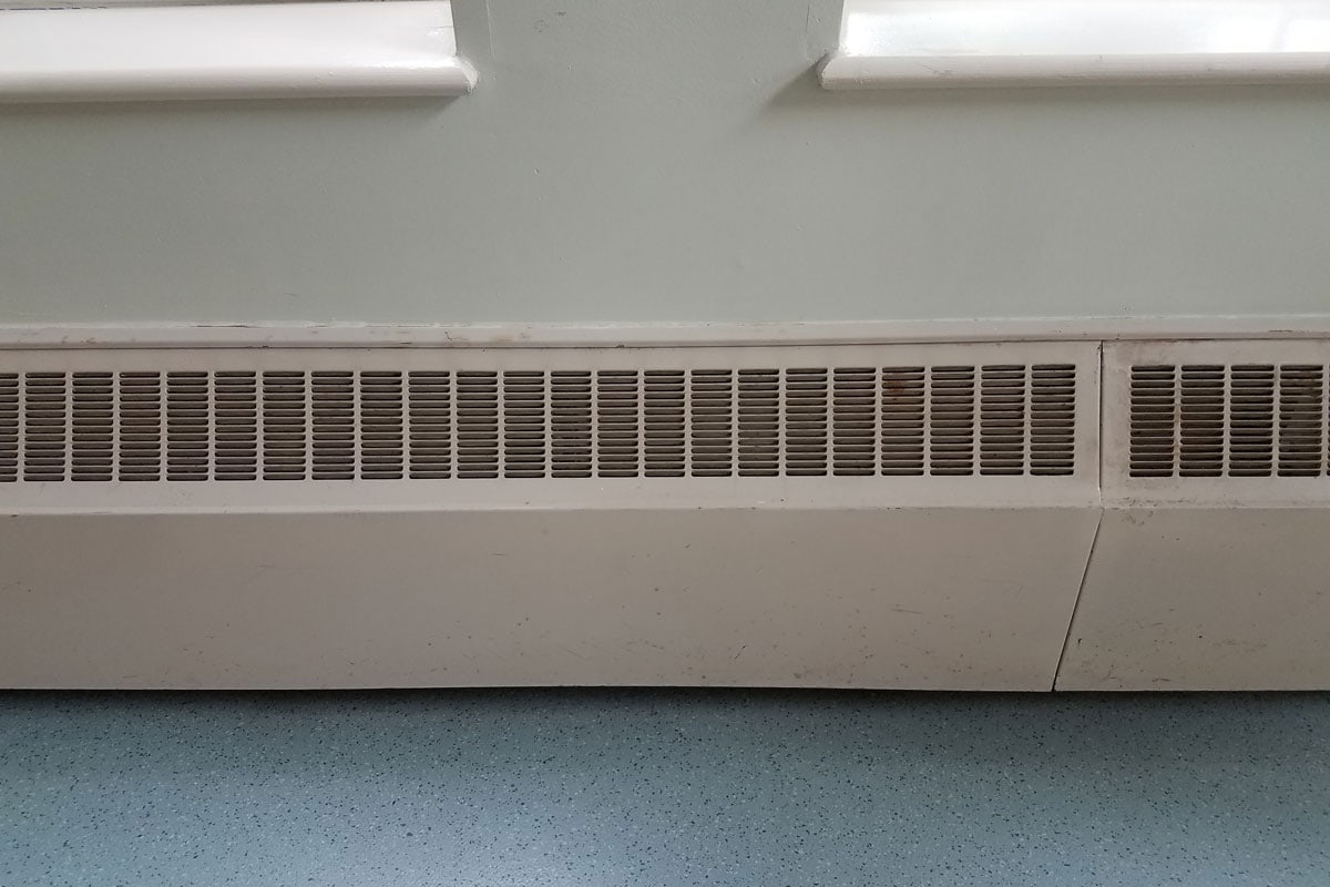 photo of a baseboard heater mounted on the wall near floor carpet green
