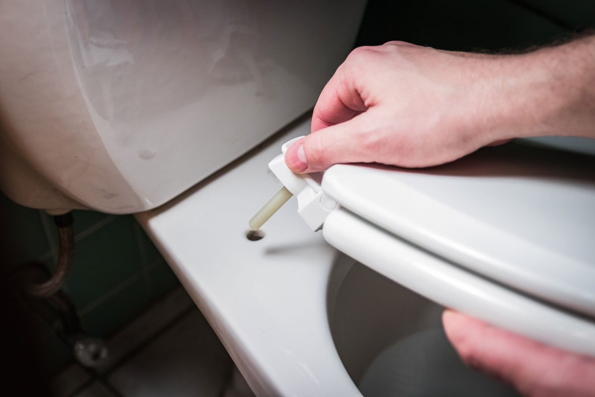 photo of a man hands installing a toilet seat on a toto toilet inside the bathroom