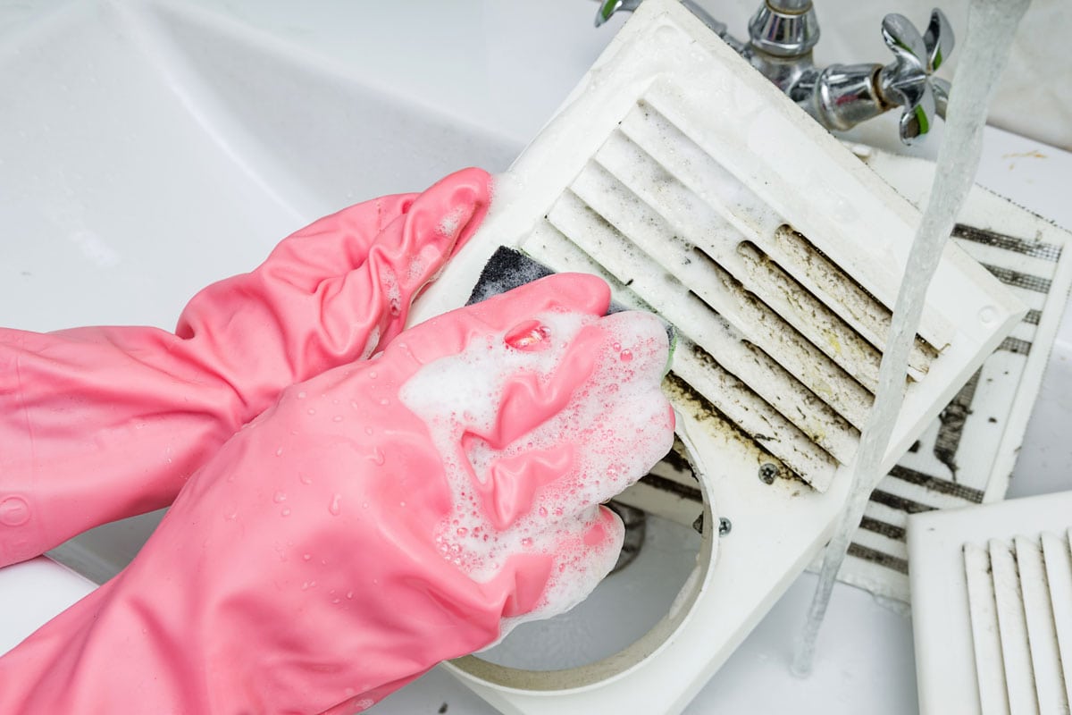 photo of a man hands wearing pink plastic gloves washing the white dirty air vents cleaning