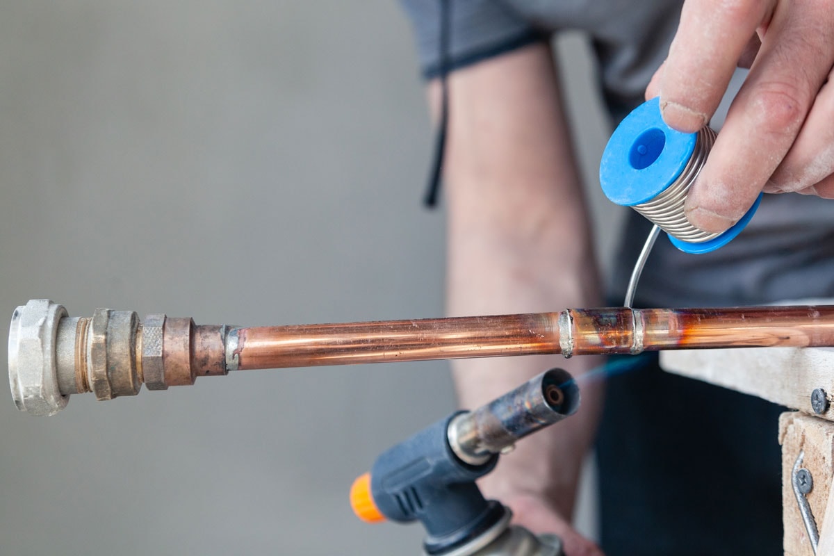 photo of a man soldering a copper pipe for water system using a blow torch