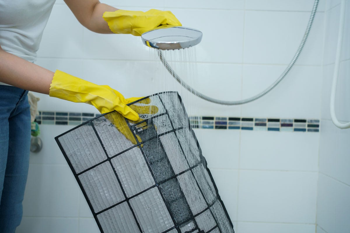 photo of a woman wearing a yellow gloves cleaning a clogged up air filter