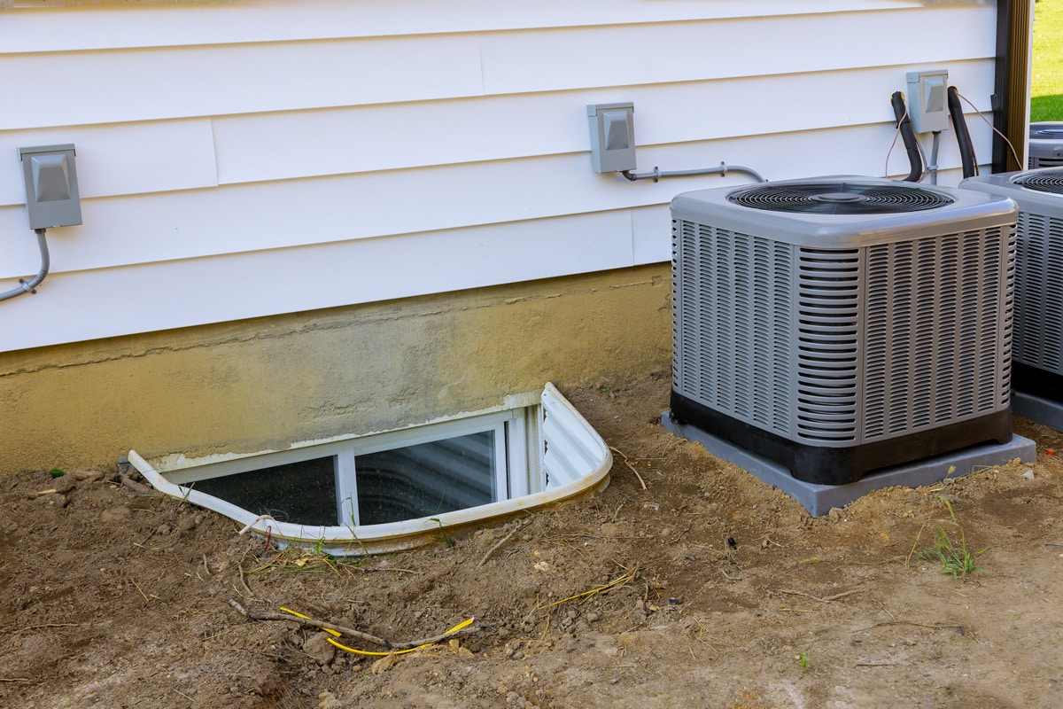 A Rheem Air conditioner on the side of a house placed on a plastic pad