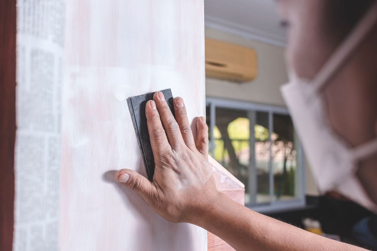 A handyman using a piece of sandpaper to smoothen out the side of a wall cabinet prior to painting. Home renovation or finishing works.