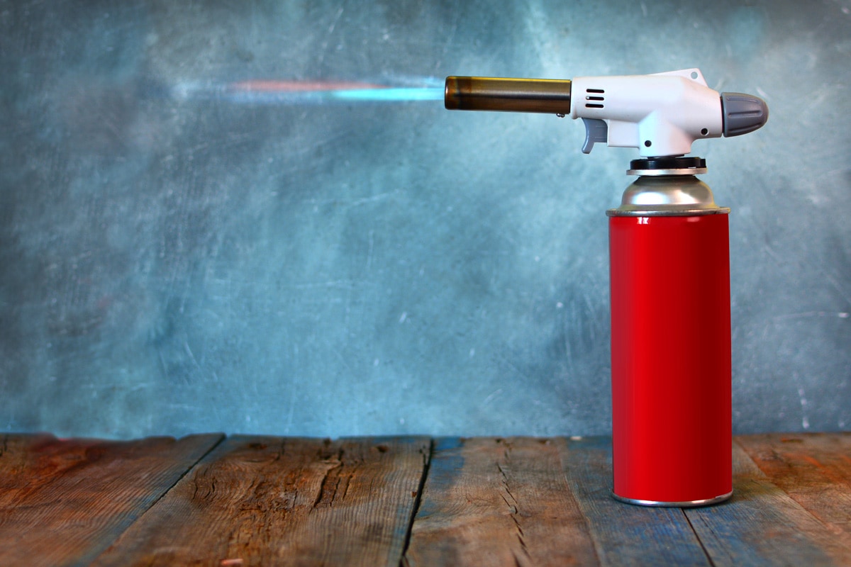 A red colored butane torch placed on the table