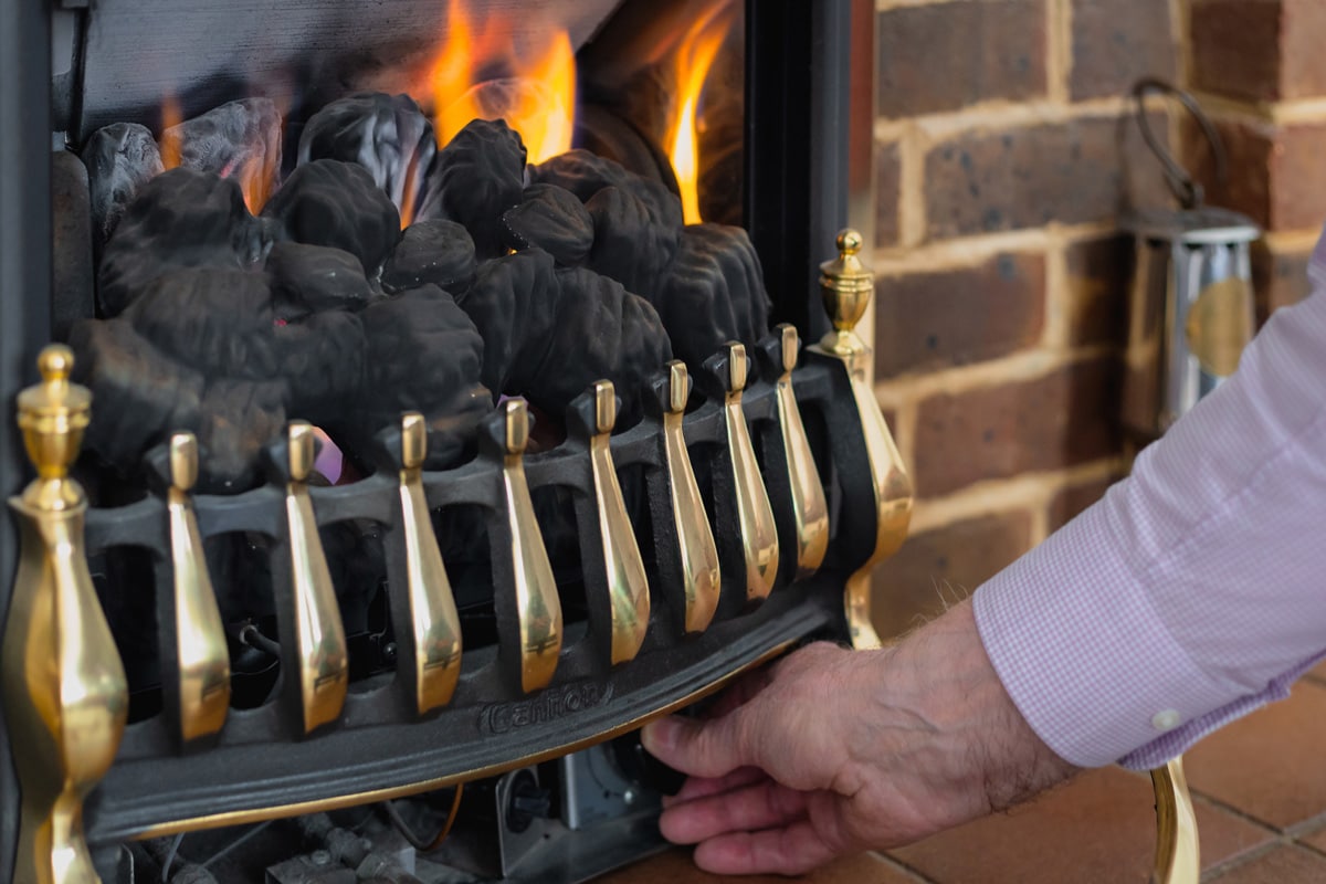 A senior man turning down the heat, and saving energy, on his gas fire at home by adjusting the knob. Room for copy space.
