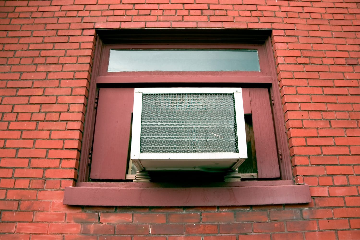 A small air conditioner in the window of a brick apartment building.