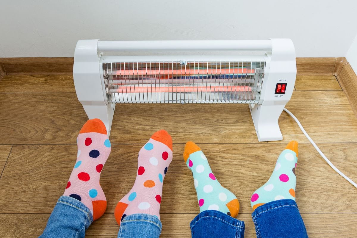 A young family wearing bright polka dot socks warms their cold feet near an electric heater. Infrared halogen heater at home.