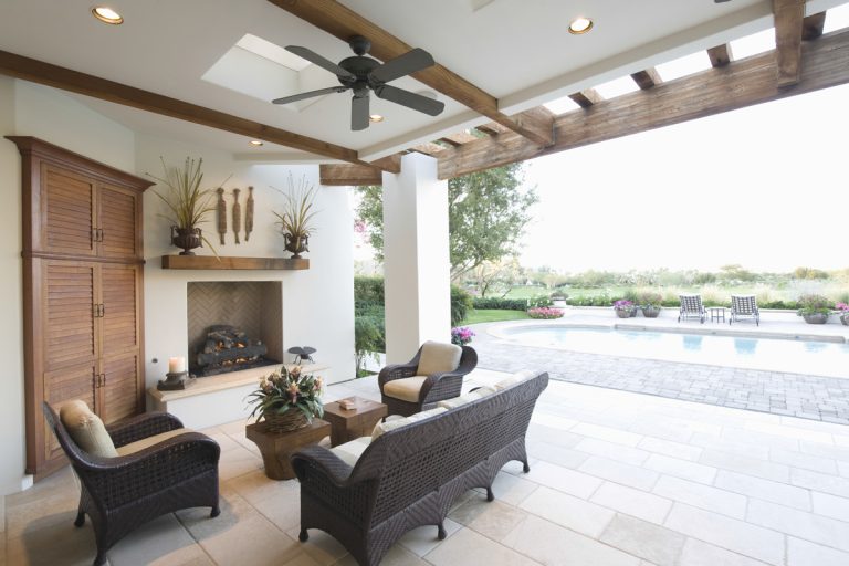 Bohemian inspired outdoor entertainment area with a black outdoor ceiling fan, wicker chairs and white painted walls with recessed lighting, Can You Use An Outdoor Ceiling Fan Indoors? Should You?