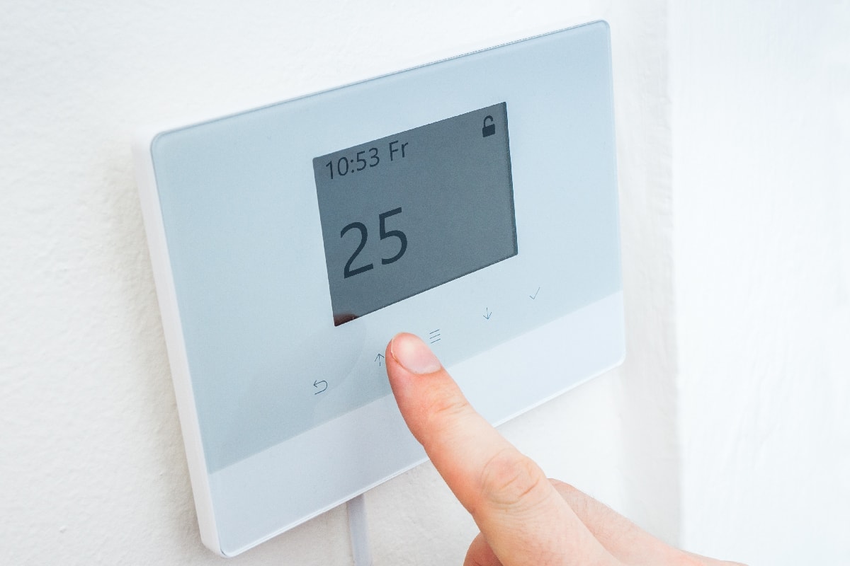 Hand is adjusting temperature in room on digital central thermostat control