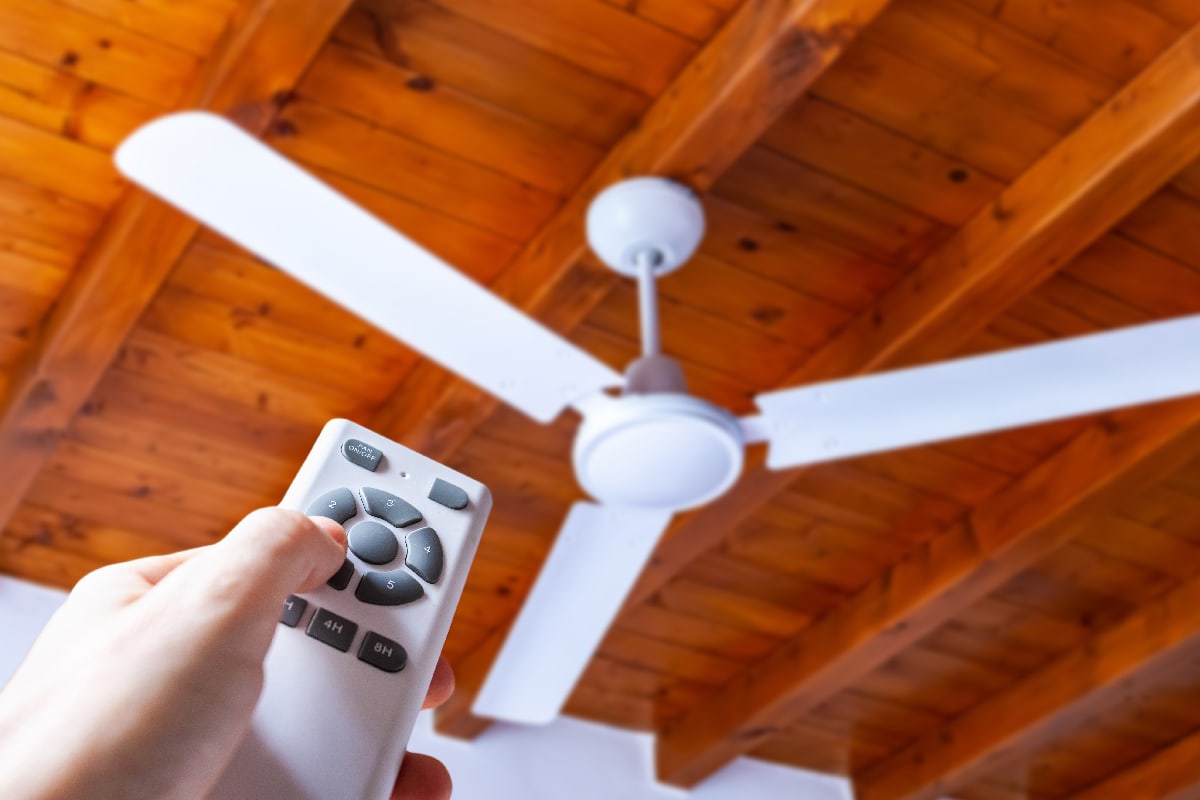 Hand using a remote control to operate a ceiling fan mounted in a hous
