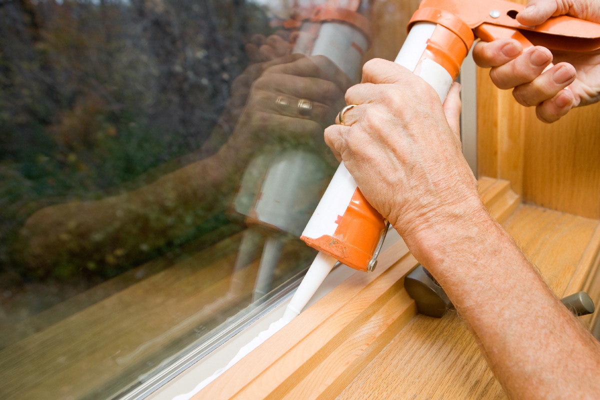 Hands applying weather seal caulk to window frame