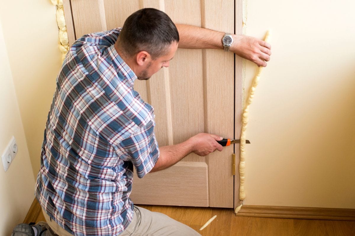 .Handyman knife cuts off excess mounting foam. Installation of doors using polyurethane foam mounting.