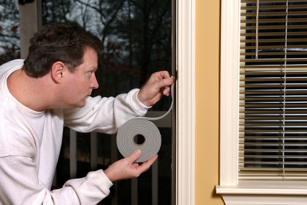 Homeowner applying weather stripping to stop air leaks around a doorway.