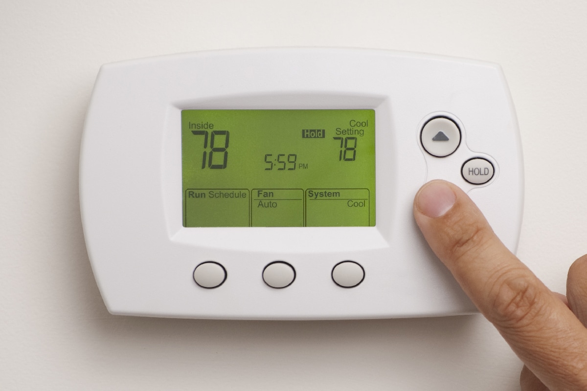 Male hand on digital thermostat set at 78 degrees