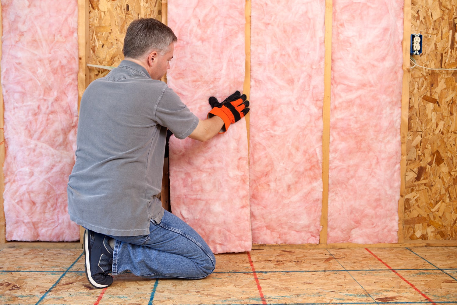 Man installing fiberglass insulation in the wall.