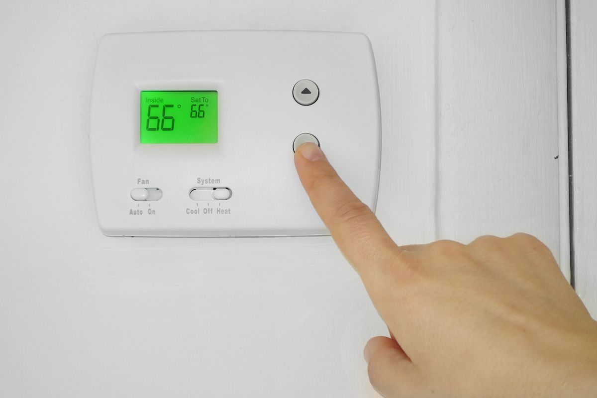 Person adjusting a wall thermostat temperature