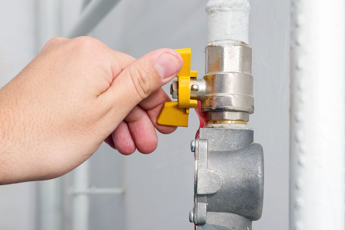Person's hand opens or closes yellow gas valve on gas pipe at home.